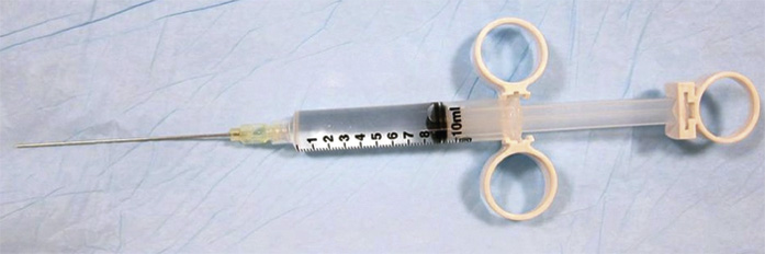 A syringe with a long attached needle placed on a sterile surface.